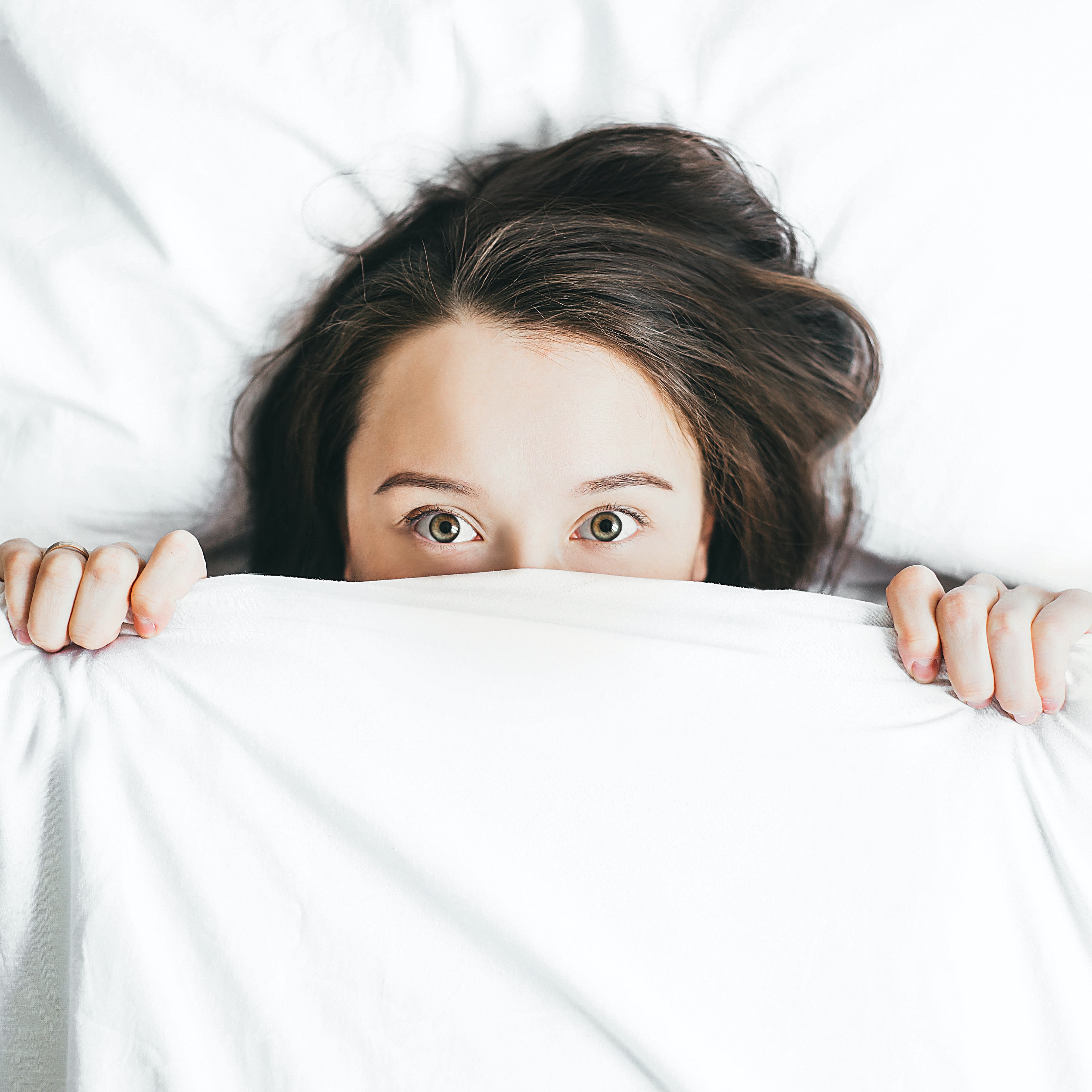 Young woman in bed with white sheets pulled up over her nose