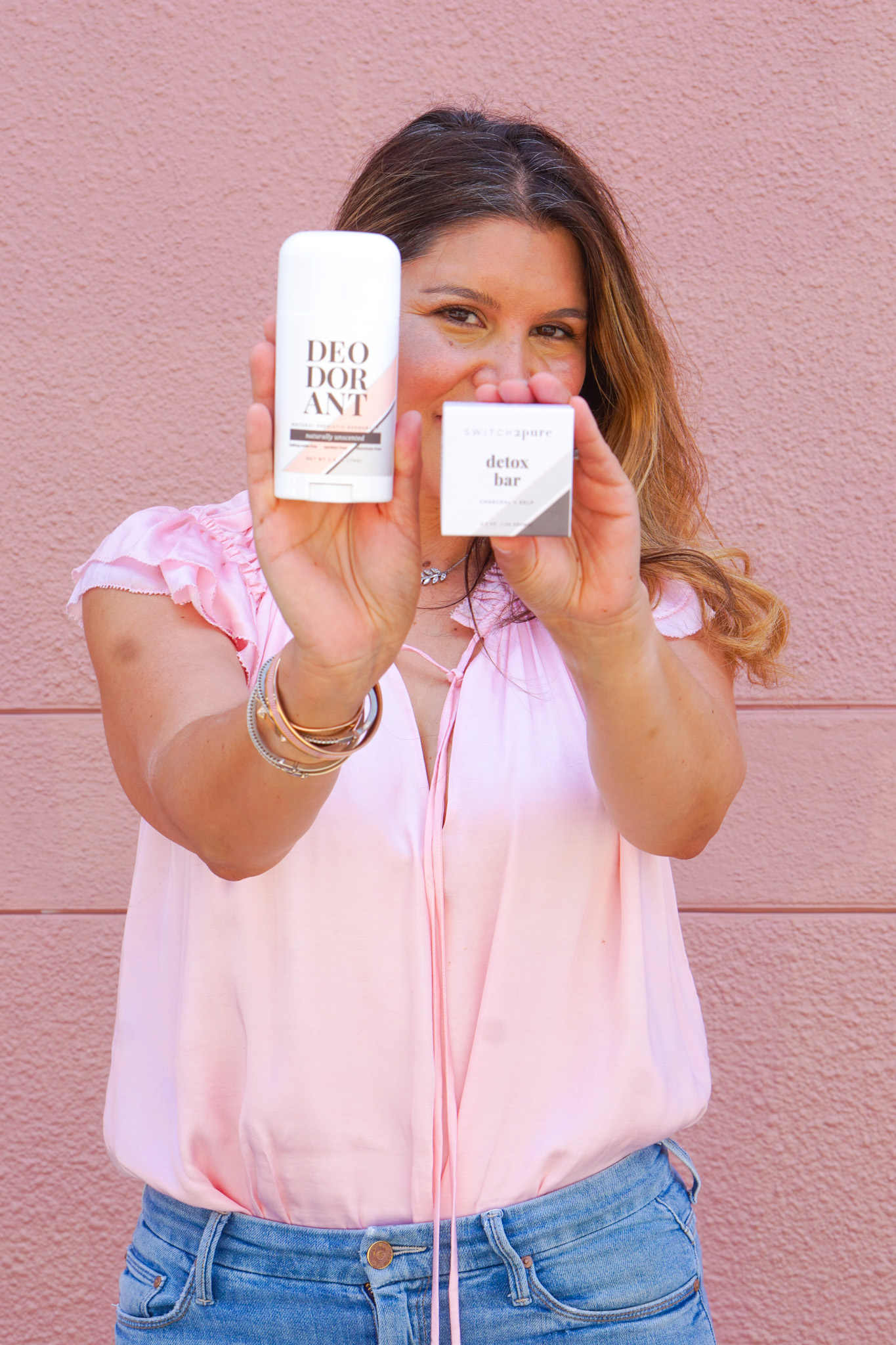 Non-Toxic Prebiotic Switch 2 Pure deodorant and Detox bar held by Founder Estela with a pink wall background