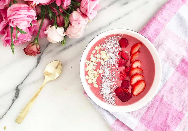 Chia parfait bowl with almonds, coconut flakes, raspberries and strawberry slices, gold spoon next to bowl with a bouquet of pink and white roses in the upper left corner